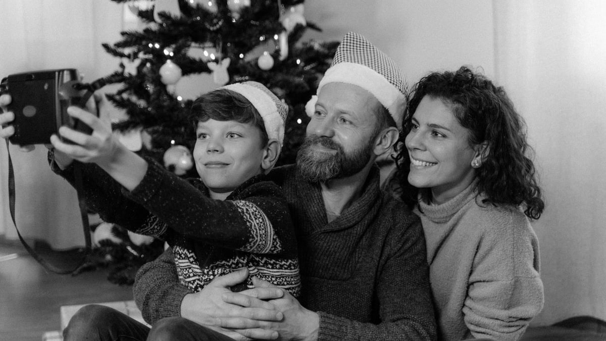 A joyful family takes a Christmas selfie with an instant camera beside a decorated tree.
